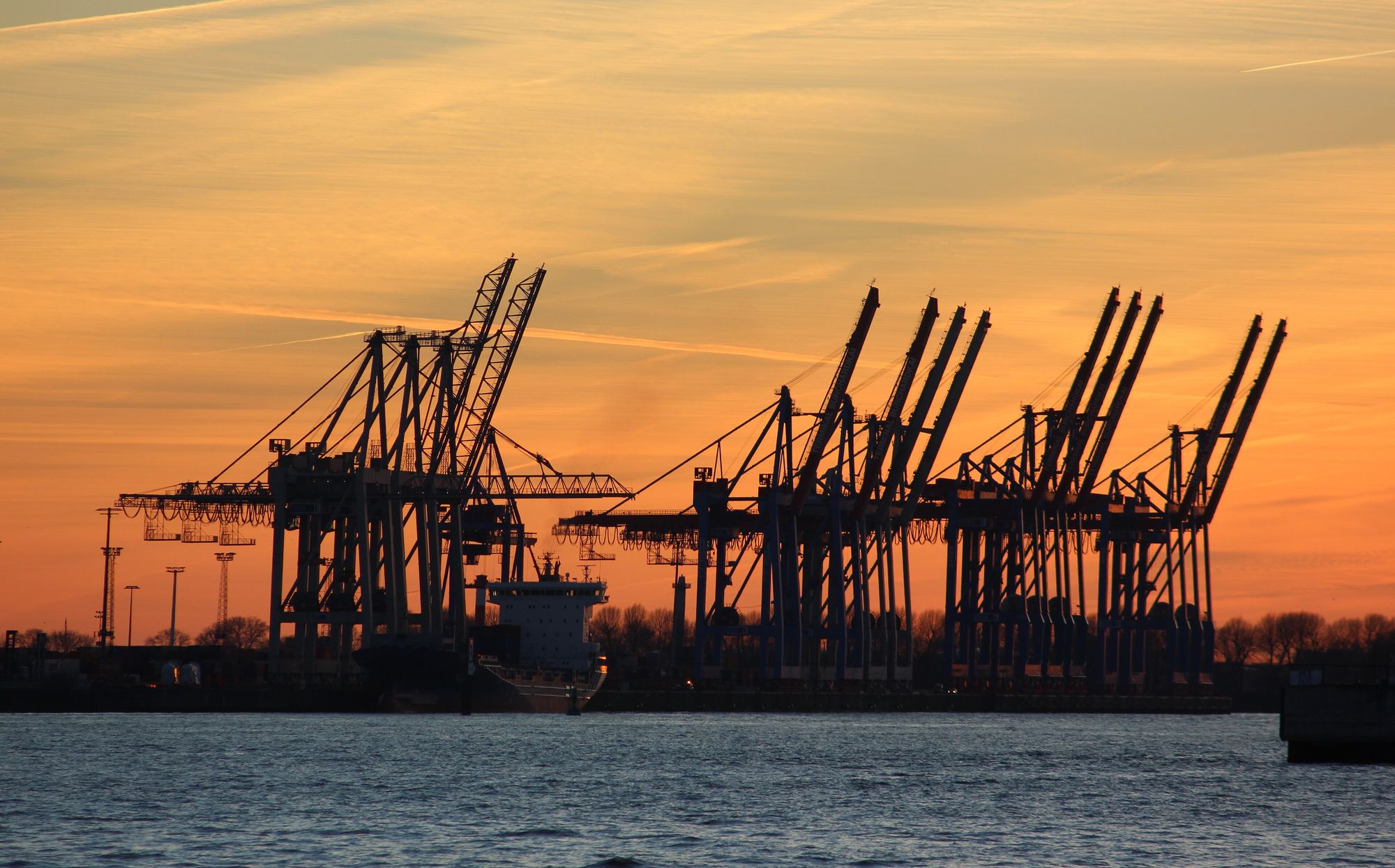 Container cranes silhouetted against a golden sunset in the Port of Hamburg